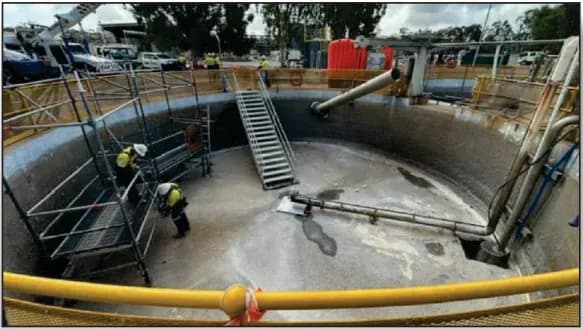 Operarios realizando trabajos de mantenimiento y aplicación de recubrimiento protector en las paredes internas de un gran estanque circular de hormigón en una planta industrial.