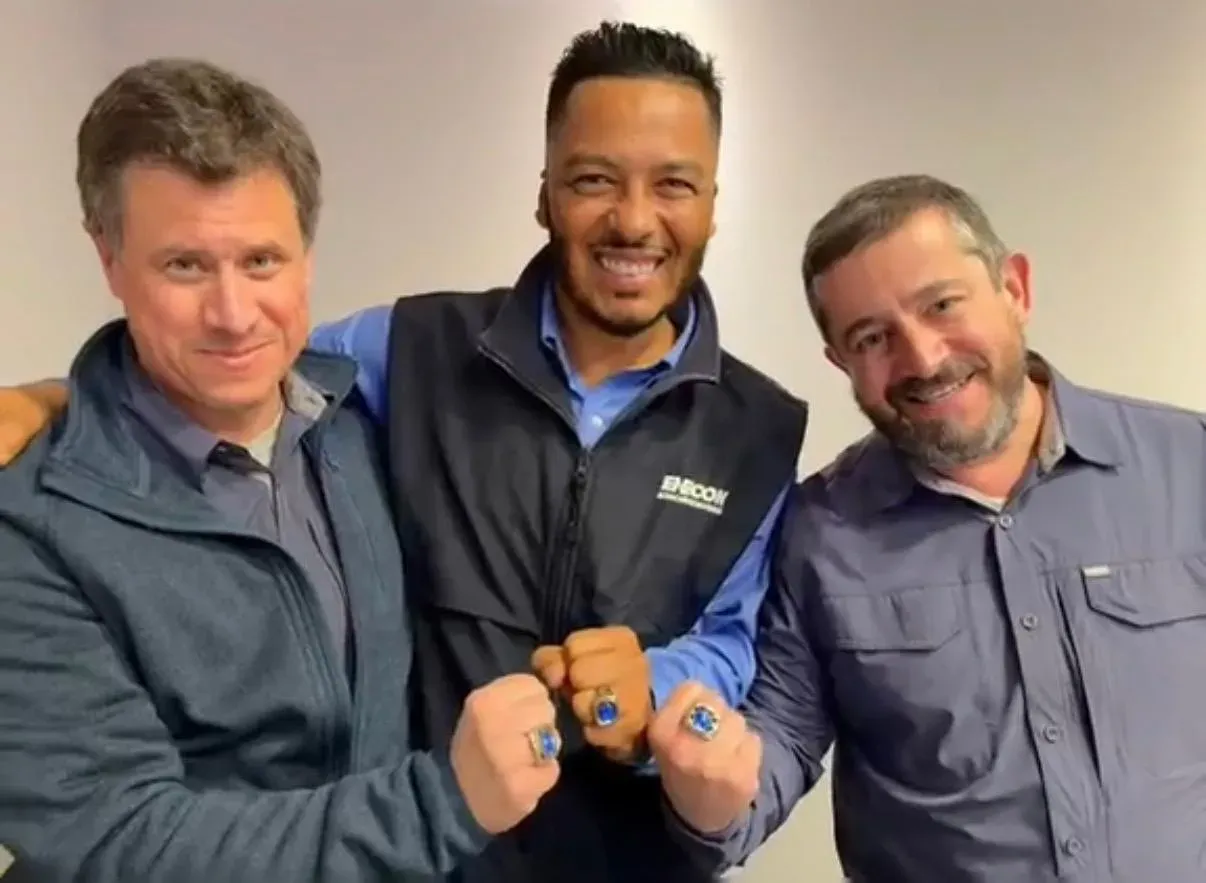 Tres representantes de ENECON Chile sonriendo y mostrando anillos de reconocimiento corporativo con piedras azules en sus puños cerrados.