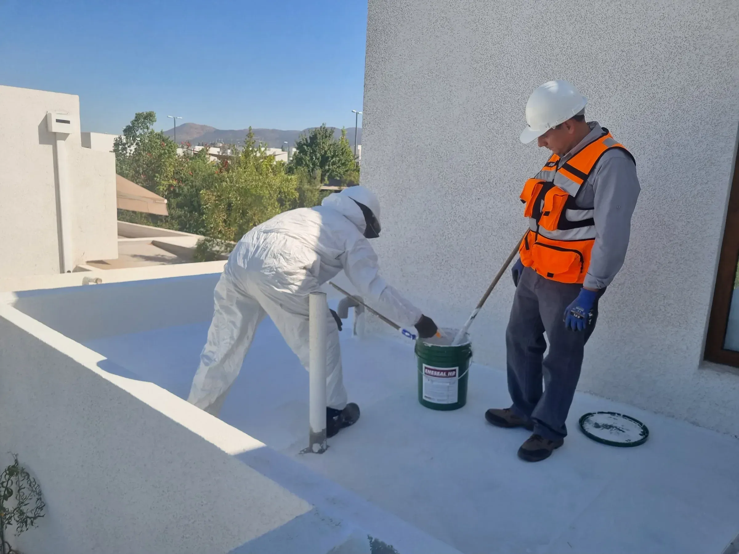 Aplicación de recubrimiento impermeable ENESEAL HR en la techumbre de un edificio en La Dehesa, con operarios preparando la membrana polimérica blanca de alta reflectividad.