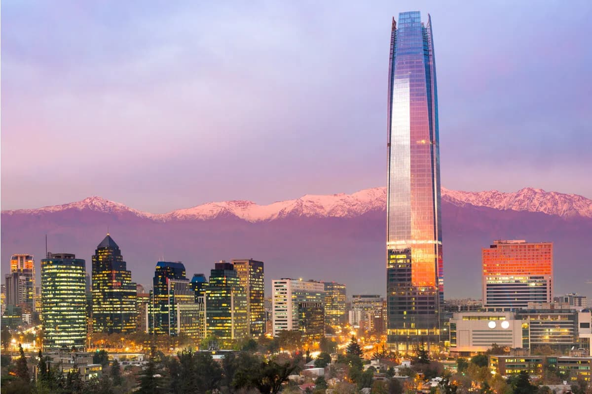 Vista panorámica de Santiago de Chile al atardecer, destacando la Gran Torre Santiago y la Cordillera de los Andes nevada al fondo.