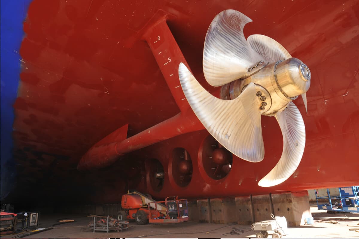 Hélice metálica pulida instalada en el casco rojo de una embarcación en dique seco, lista para recibir recubrimiento protector contra la cavitación y corrosión marina.