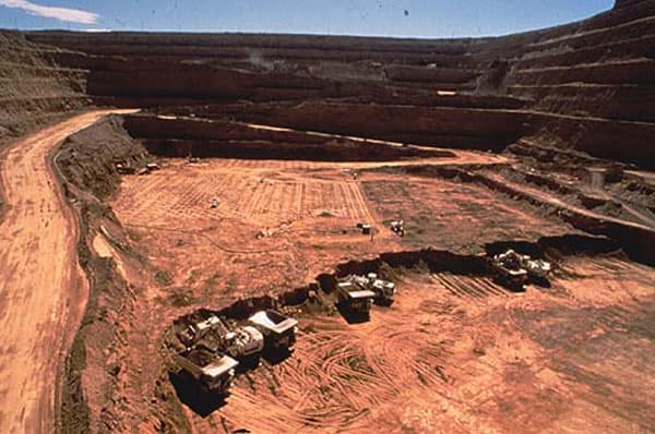 Vista panorámica de una mina a rajo abierto con camiones de extracción operando en el fondo, expuestos a condiciones extremas de abrasión y desgaste.
