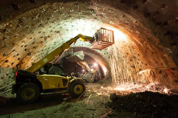 Manipulador telescópico con canastillo en túnel de minería subterránea, donde un operario realiza trabajos de soldadura generando chispas bajo la bóveda reforzada.