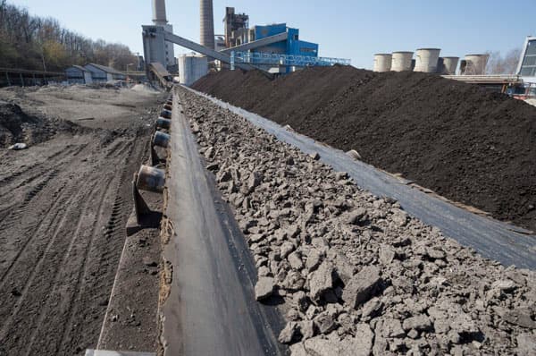 Correa transportadora cargada con mineral triturado en una planta de procesamiento minero, expuesta a alta abrasión y desgaste continuo.
