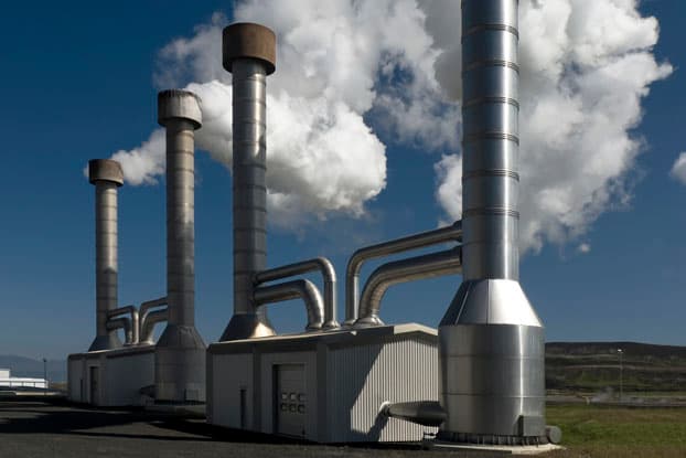 Chimeneas metálicas de una planta de generación de energía emitiendo vapor blanco bajo un cielo azul, expuestas a la intemperie y altas temperaturas.