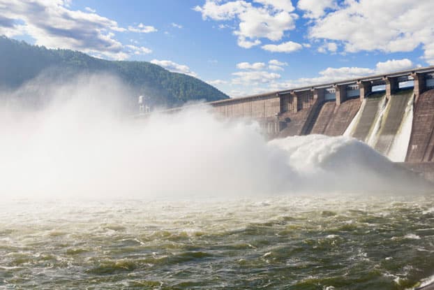 Represa hidroeléctrica liberando un gran caudal de agua con alta turbulencia, propensa a problemas de erosión y cavitación en sus estructuras de hormigón.