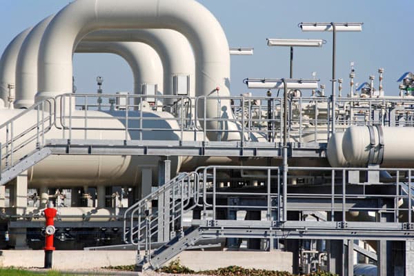 Tuberías industriales curvas de gran diámetro y tanques de almacenamiento en una planta de tratamiento de aguas residuales, con pasarelas metálicas de acceso.